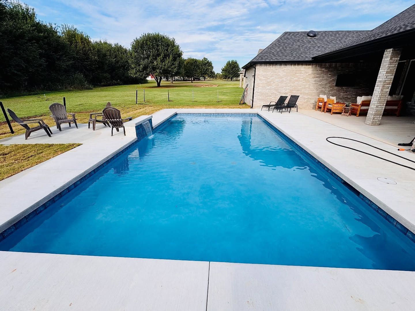 Modern backyard swimming pool with blue water, lounge chairs, and a covered patio beside a grassy lawn