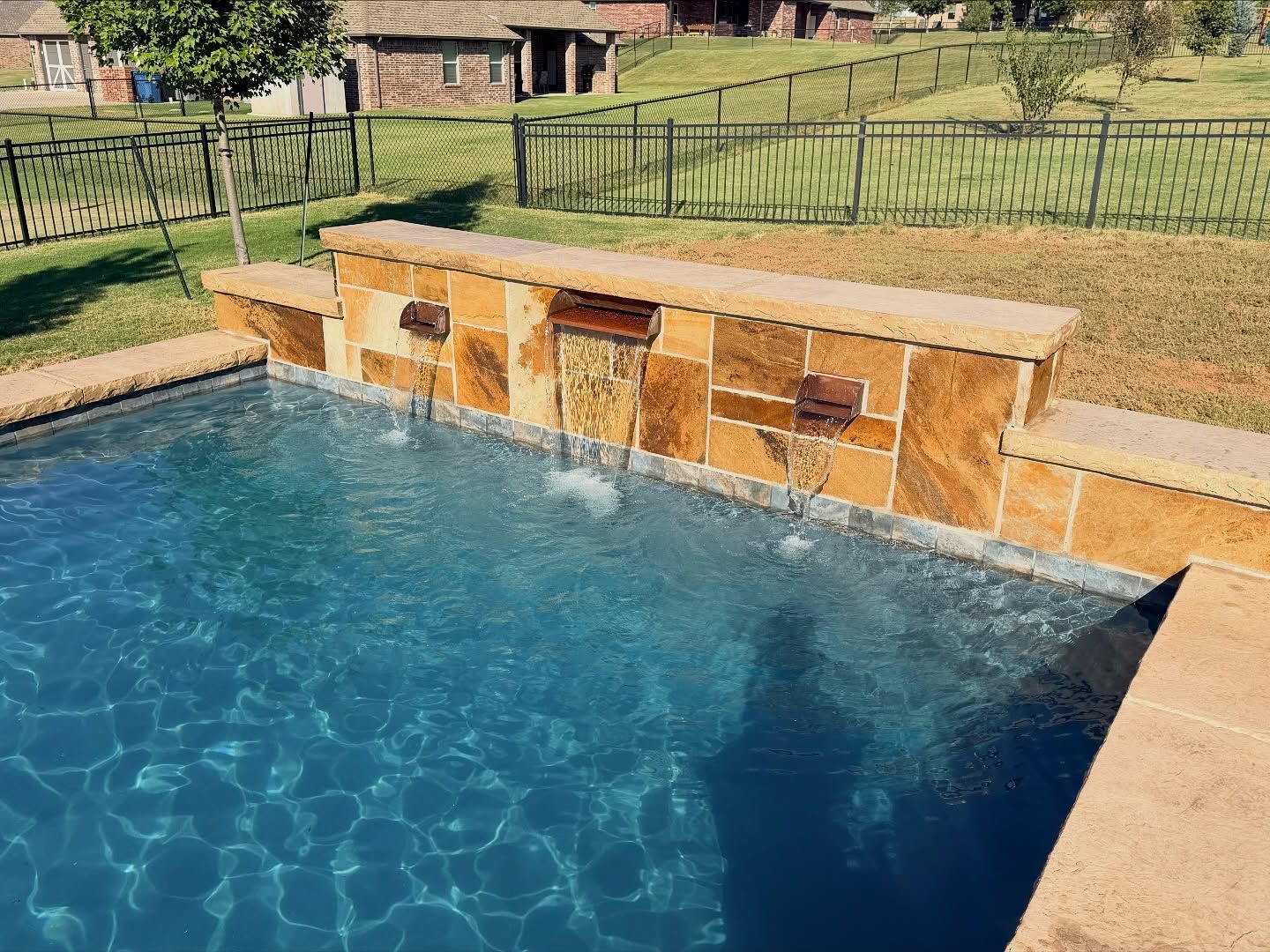 Backyard swimming pool with a tan stone waterfall fountain and blue water nearby