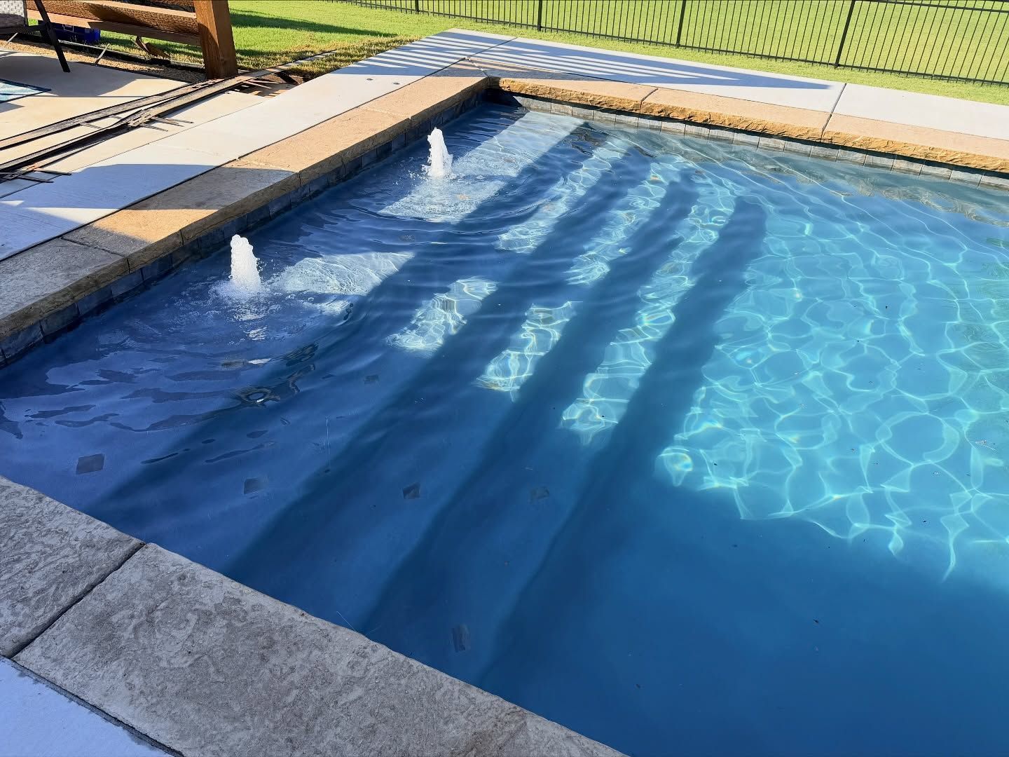 Blue swimming pool with two water jets and stone deck in sunlight