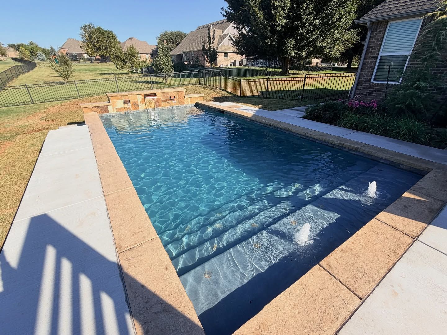 Backyard swimming pool with blue water, tan coping, and patio steps in sunny daylight