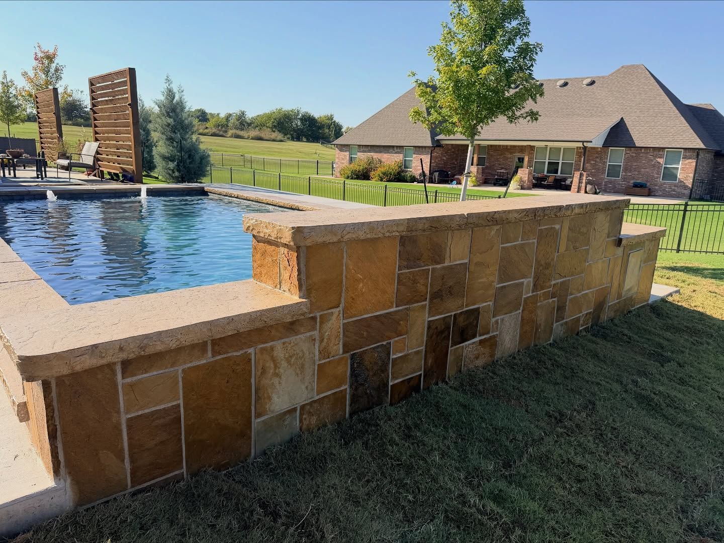 Stone pool edge beside a backyard infinity pool with grassy yard and house in the background