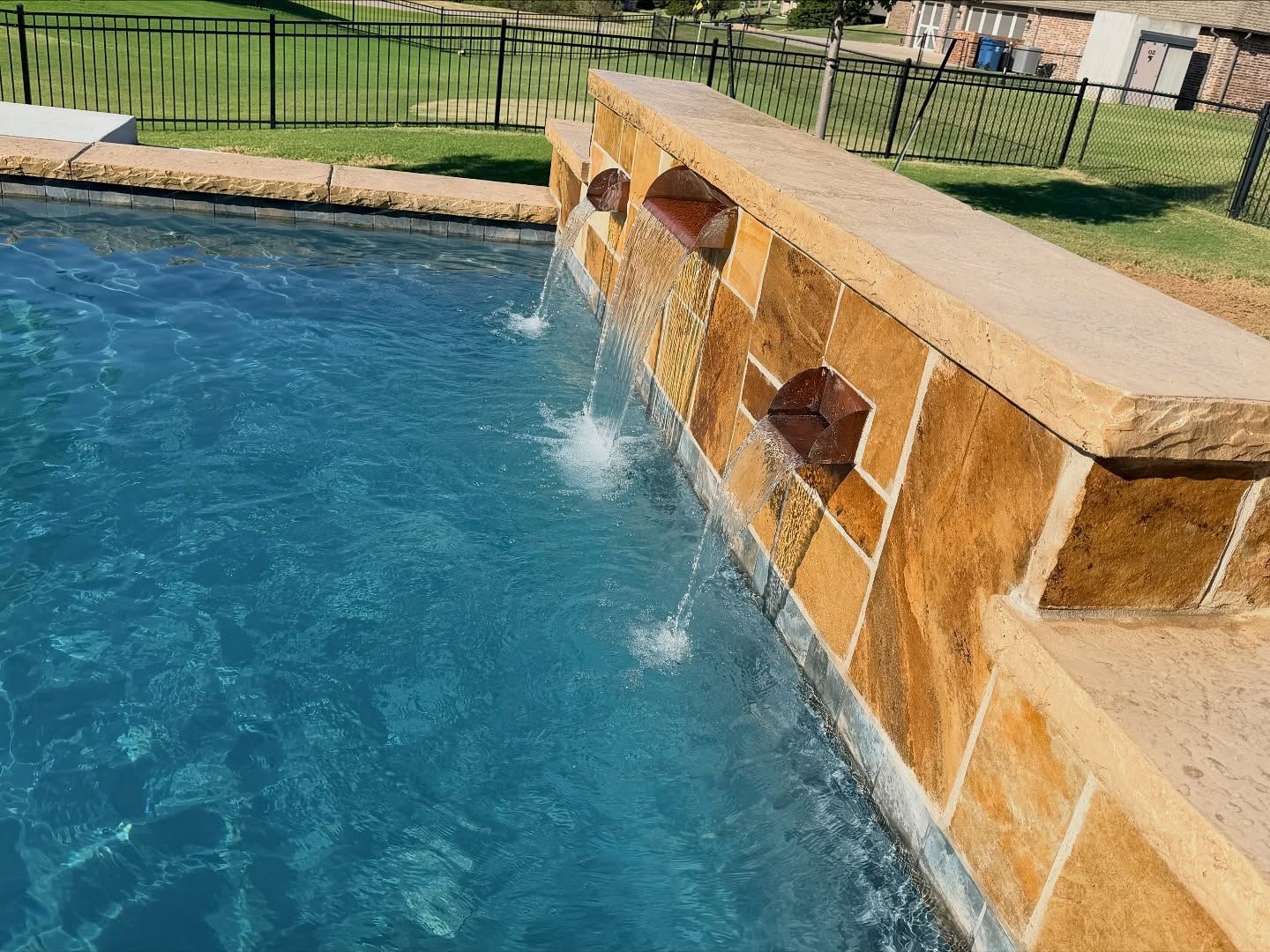 Pool waterfall spilling from a tan stone wall into clear blue water