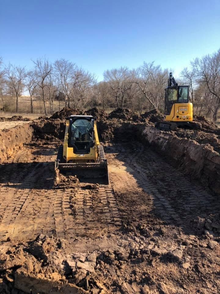 Two yellow excavators working in a muddy construction trench under a clear blue sky