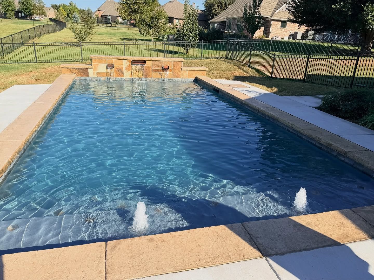 Rectangular backyard swimming pool with clear blue water, stone deck, and landscaped lawn beyond.