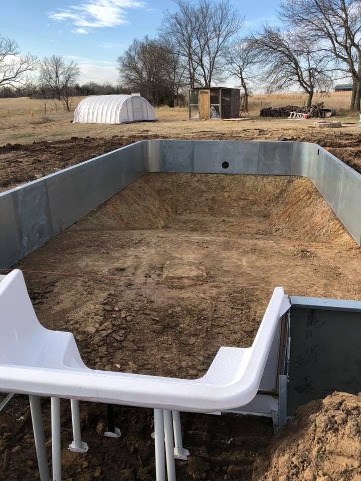 Outdoor backyard pool construction with concrete walls and a white fiberglass step, partially filled with dirt.
