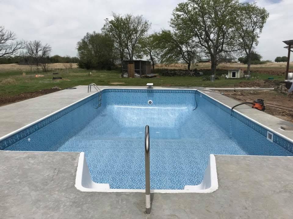 Empty blue swimming pool under construction, viewed from the shallow end in a grassy backyard.