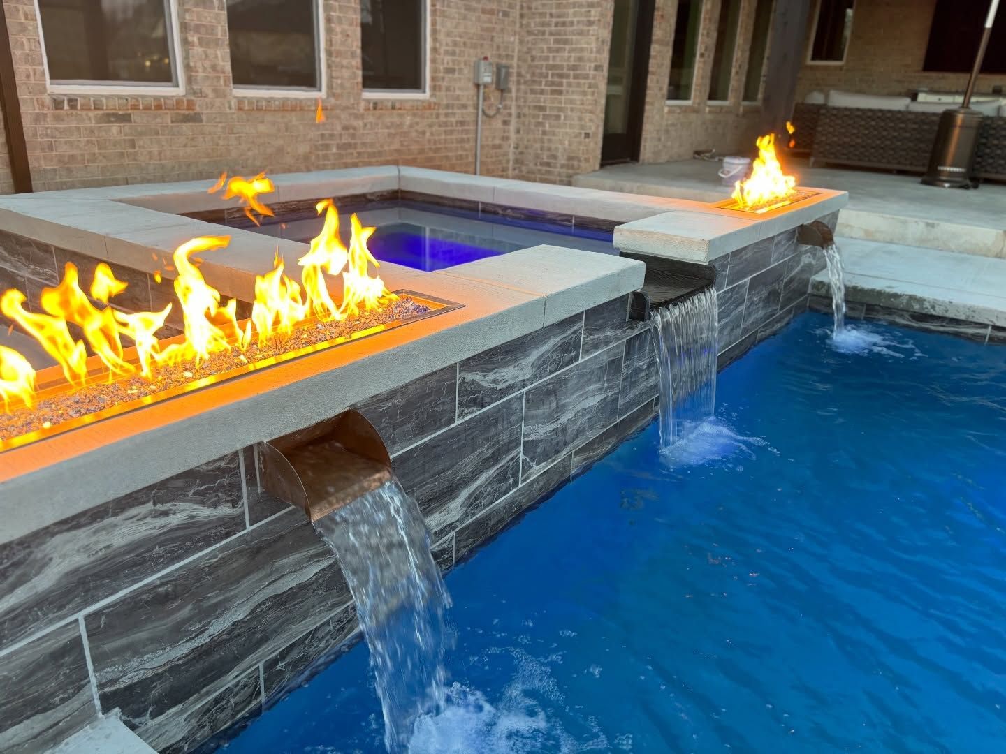 Modern fountain with fire and water features beside a blue pool