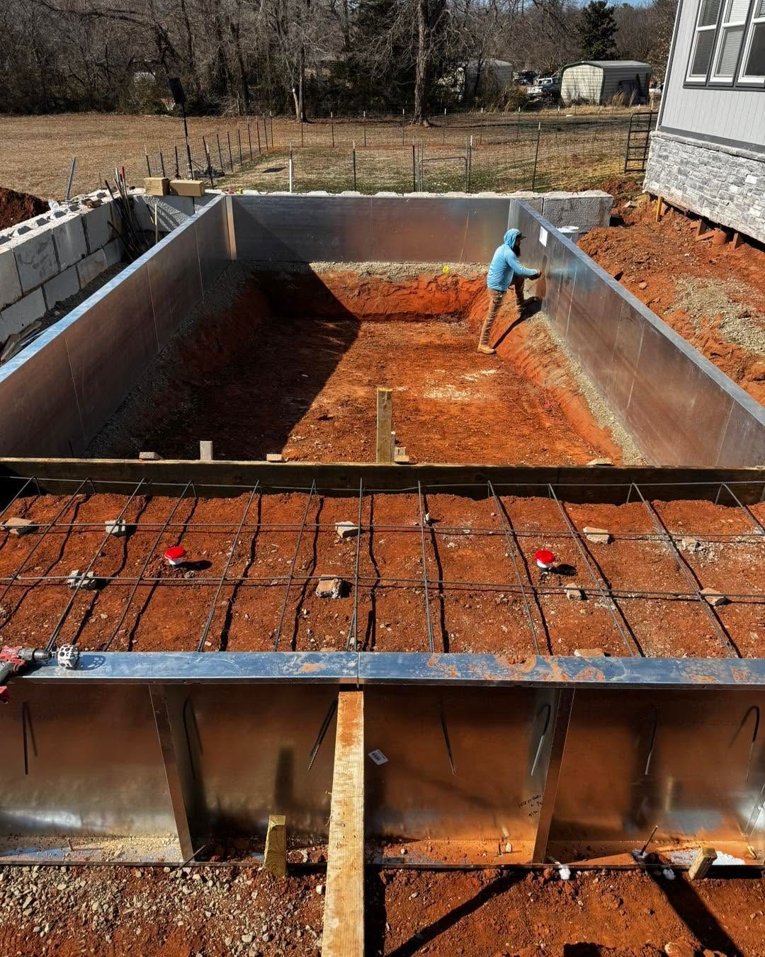 Concrete pool under construction with worker in blue shirt smoothing the floor