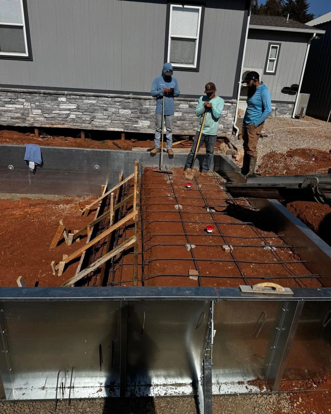 Construction workers pouring concrete around a house foundation and formwork
