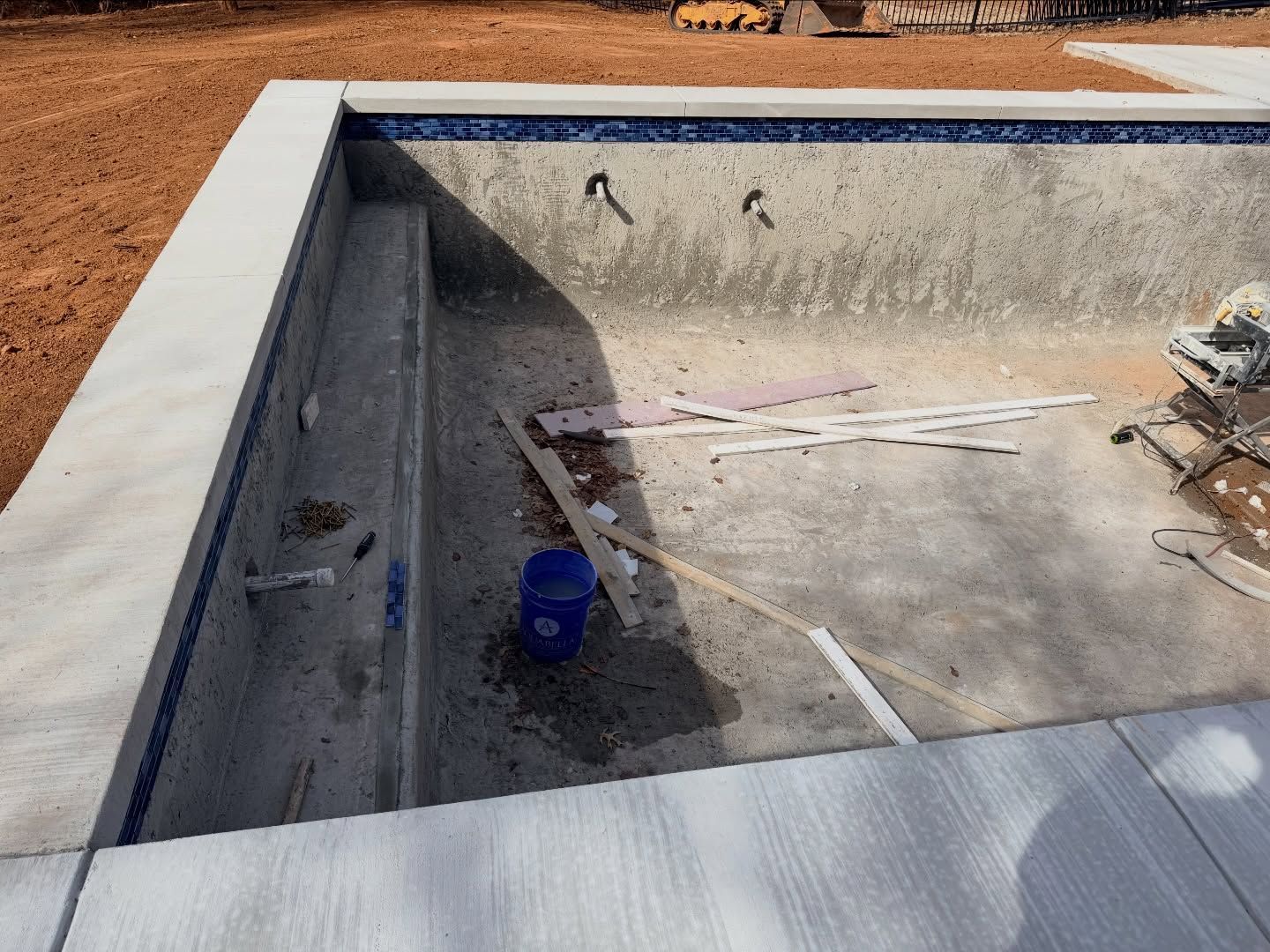 Empty concrete pool shell under construction with tools and debris inside.