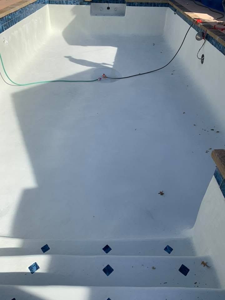 Empty white pool with blue tile accents, viewed from the shallow end under bright sunlight