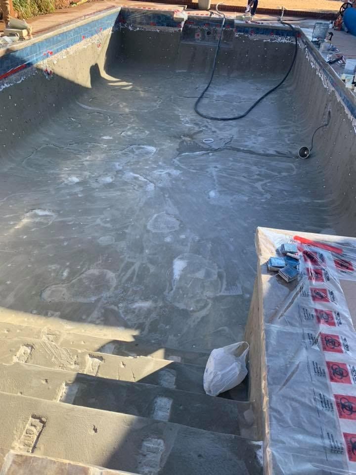 Empty concrete pool under construction with a hose and covered steps in sunlight