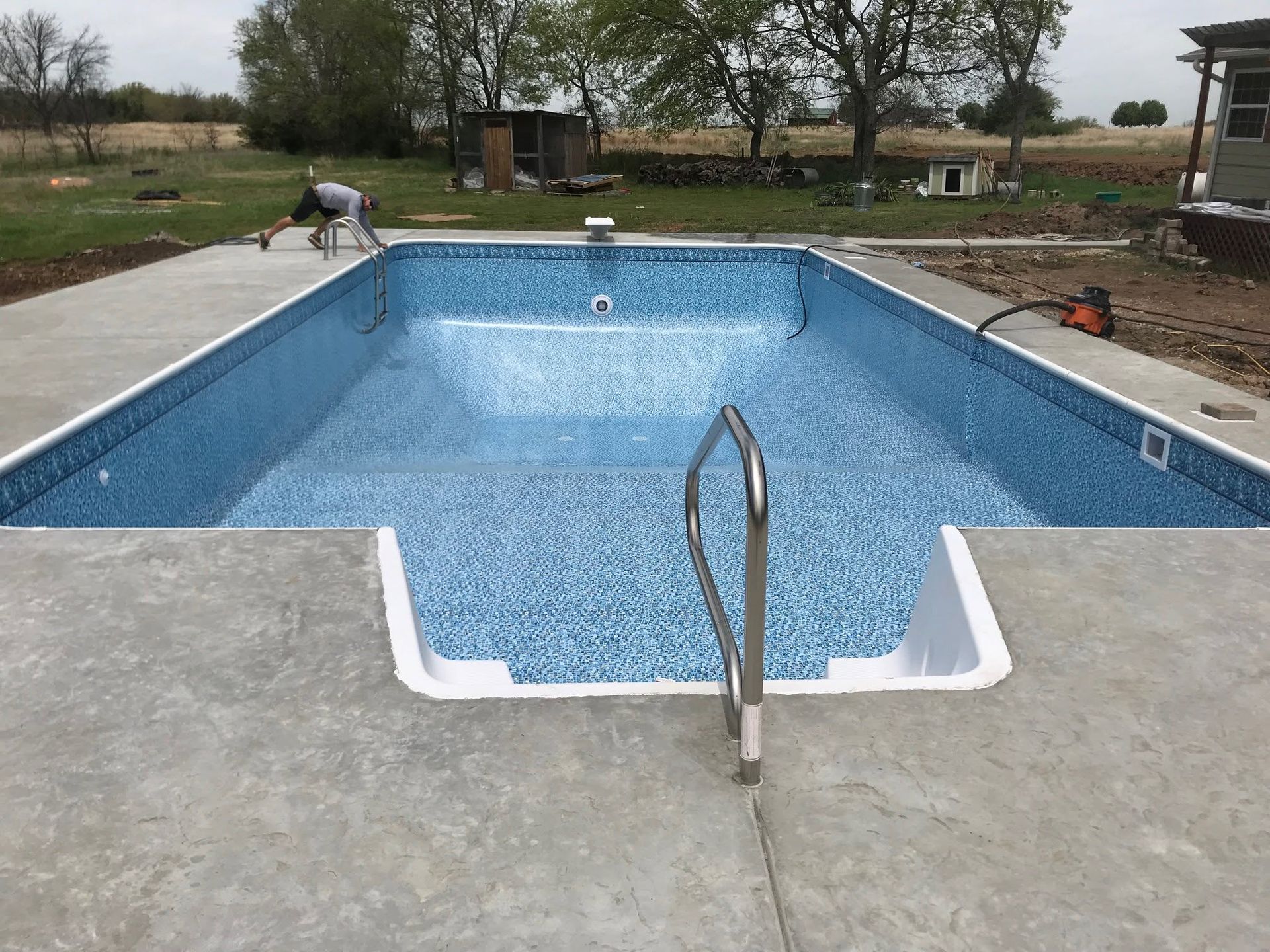 Empty rectangular swimming pool with blue tile, concrete deck, and metal handrail outdoors