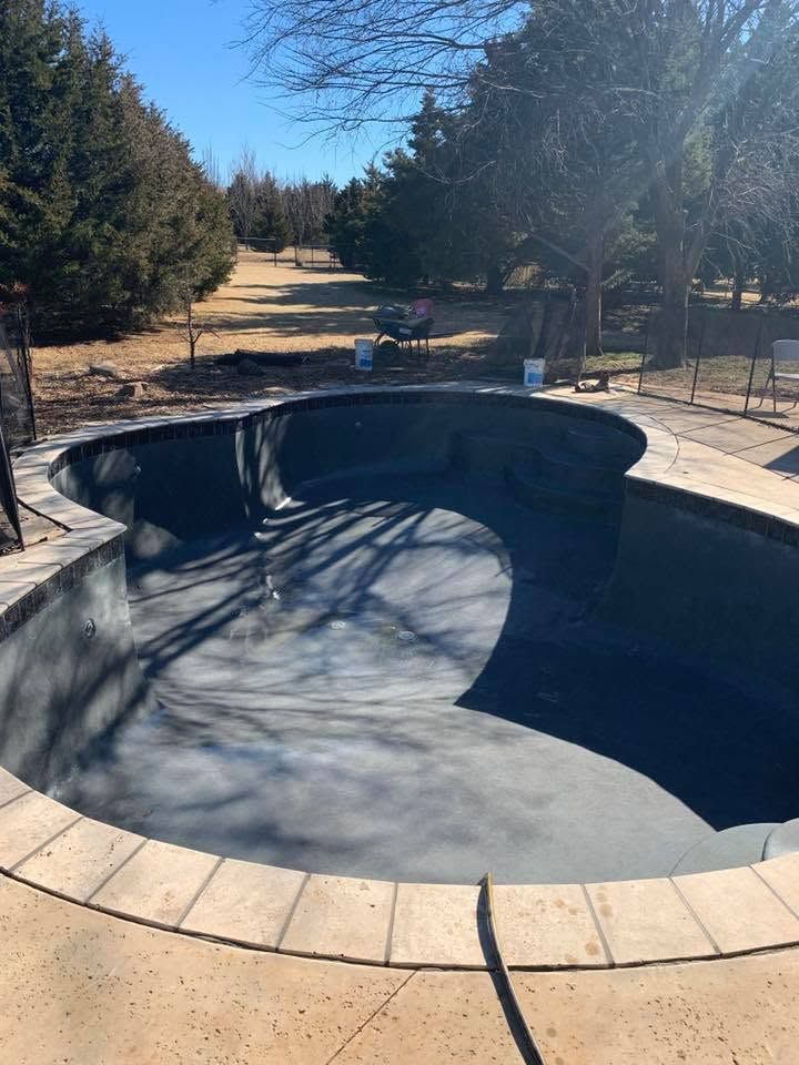 Empty backyard swimming pool in bright sunlight, surrounded by trees and patio stones.