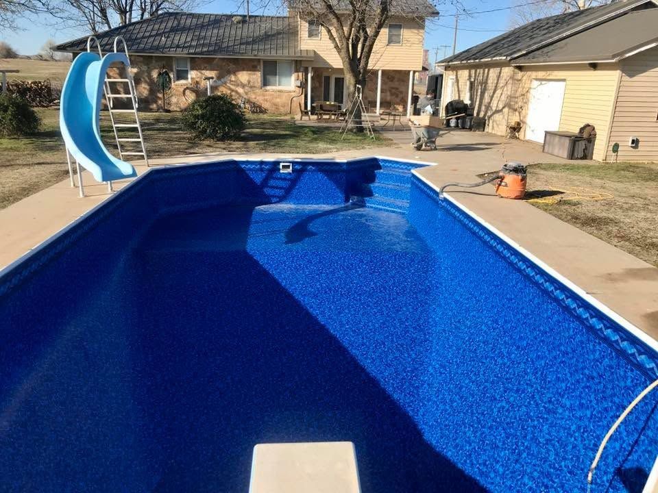 Backyard swimming pool with blue liner, slide, and house in the background