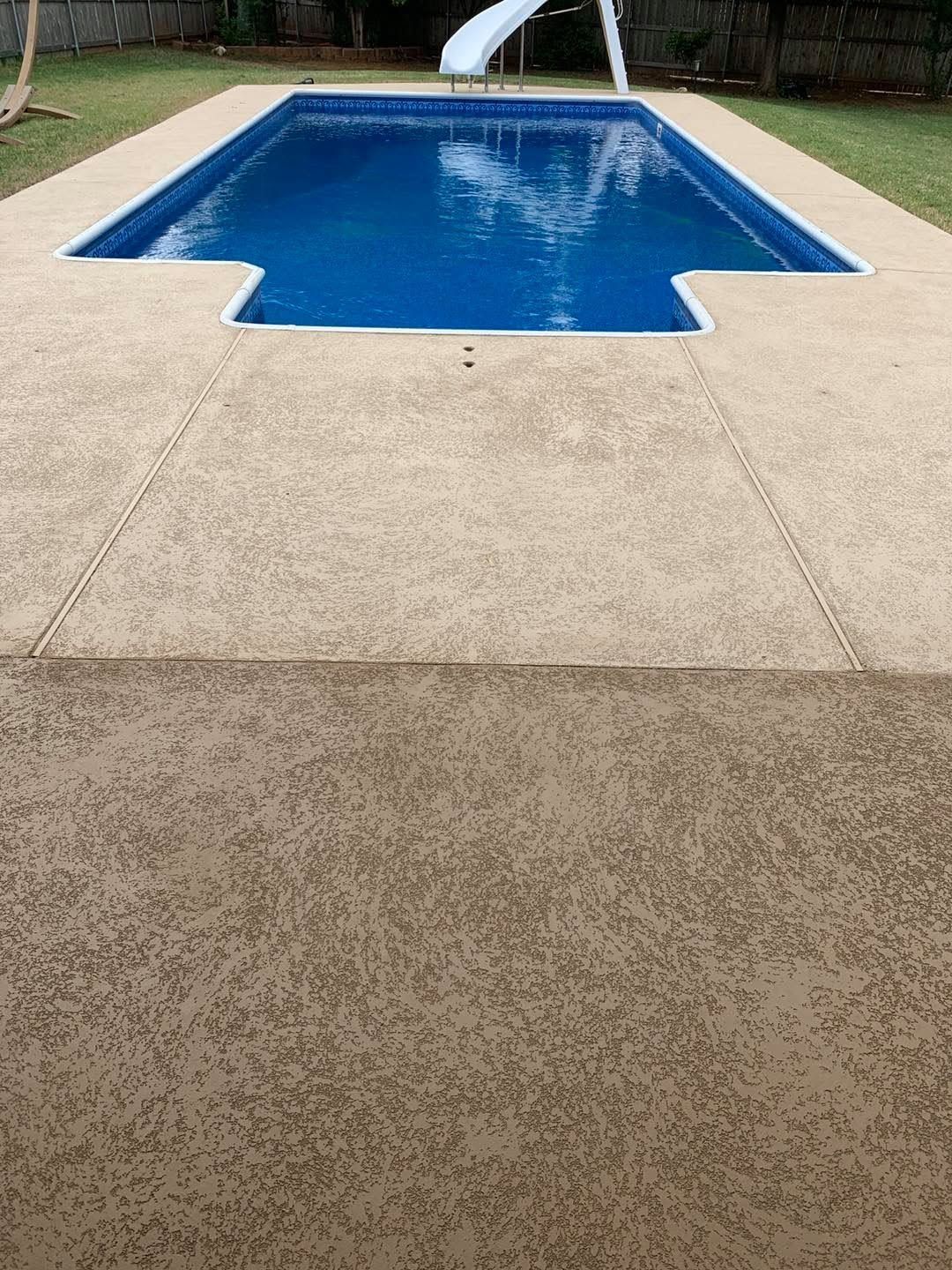 Backyard swimming pool with blue water and a beige concrete deck, viewed from the end.