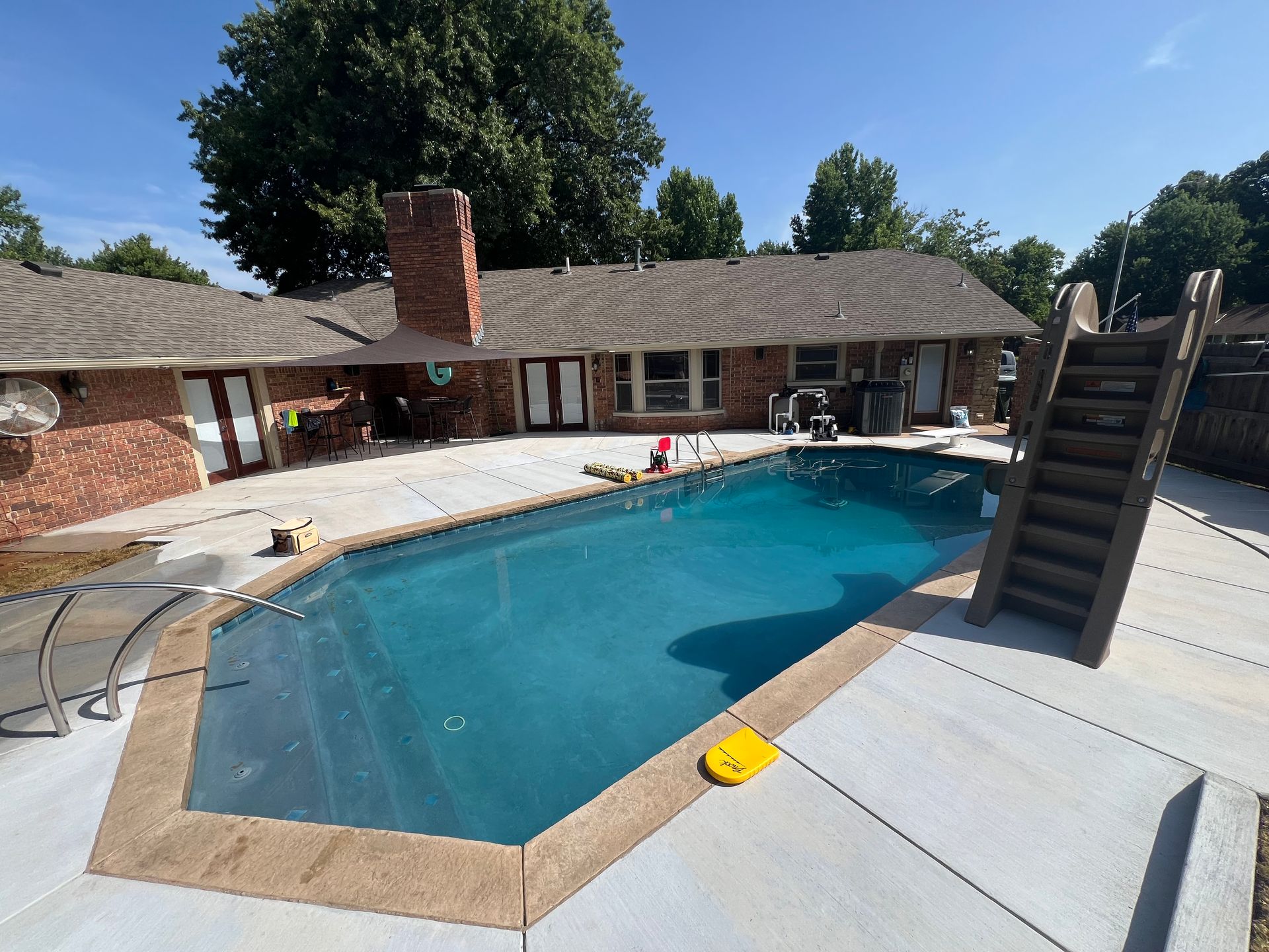 Rectangular outdoor swimming pool with turquoise water beside a brick house and parked truck under a blue sky