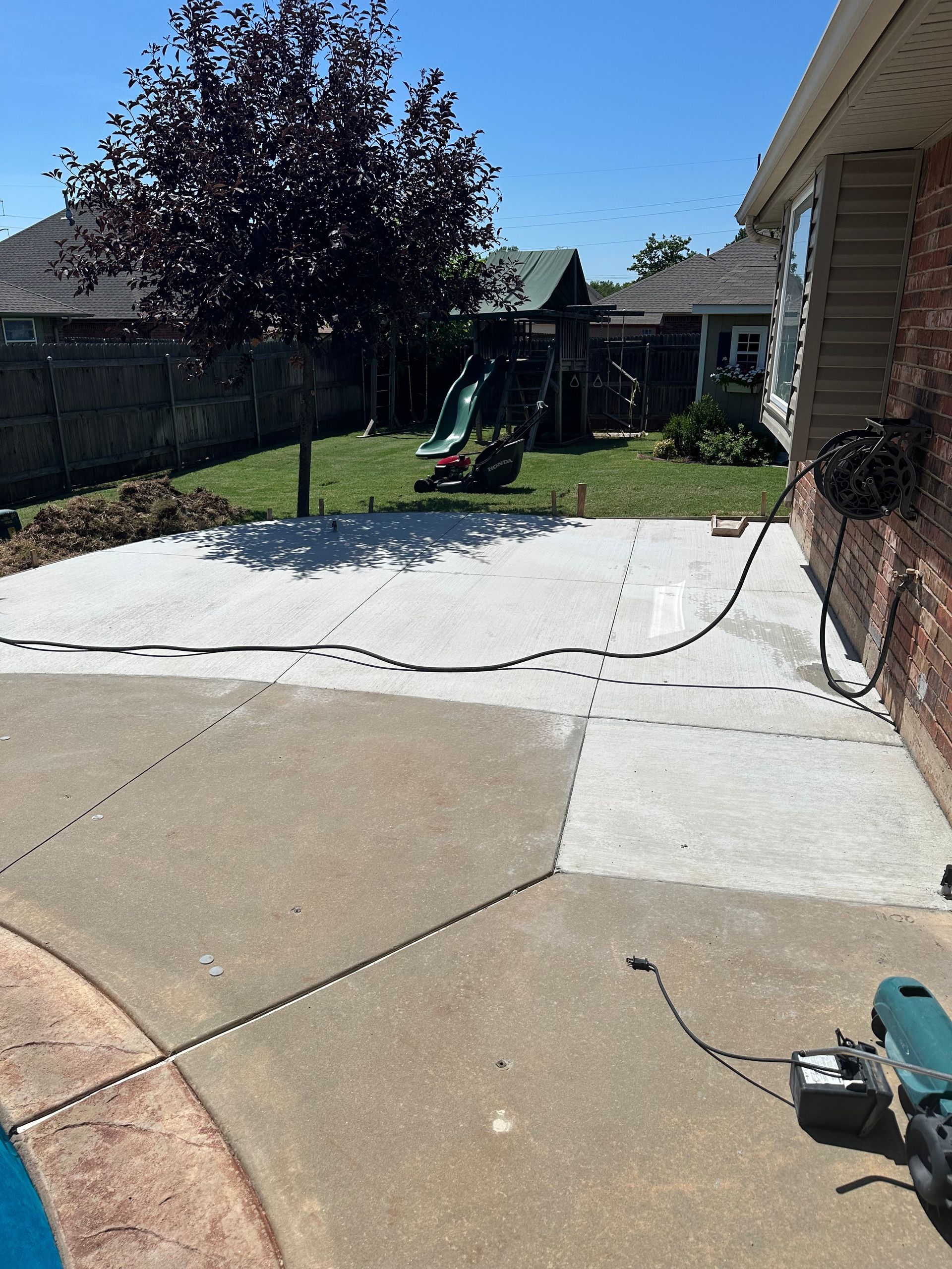 Backyard patio with a concrete slab, green slide, fence, and a pressure washer on the right.