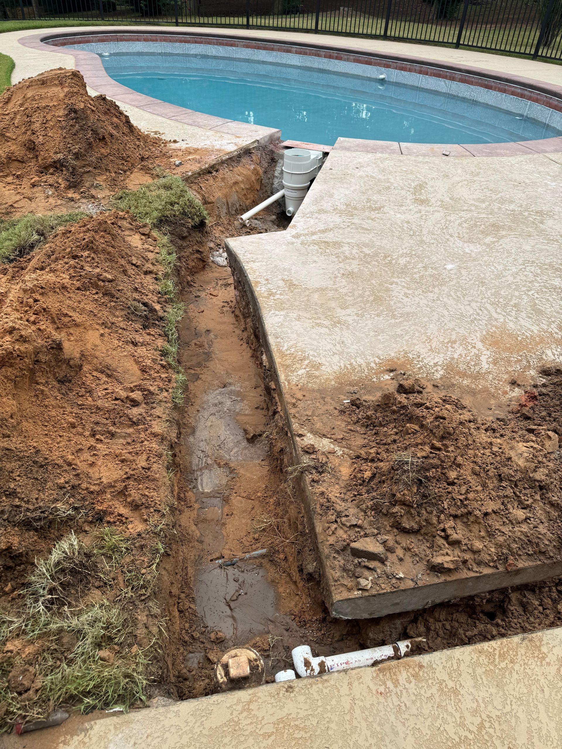 Cracked concrete pool deck with a soil trench beside a swimming pool