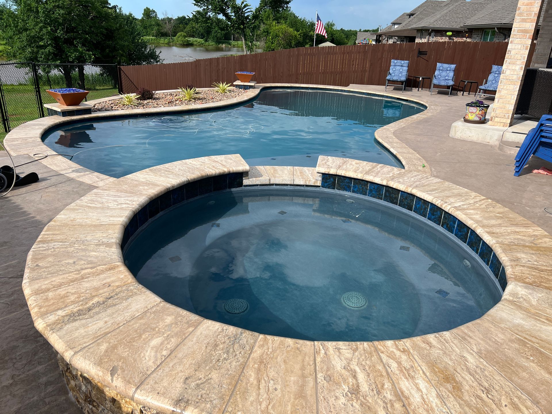 Backyard pool with a round spa, stone deck, and lounge chairs under a sunny sky