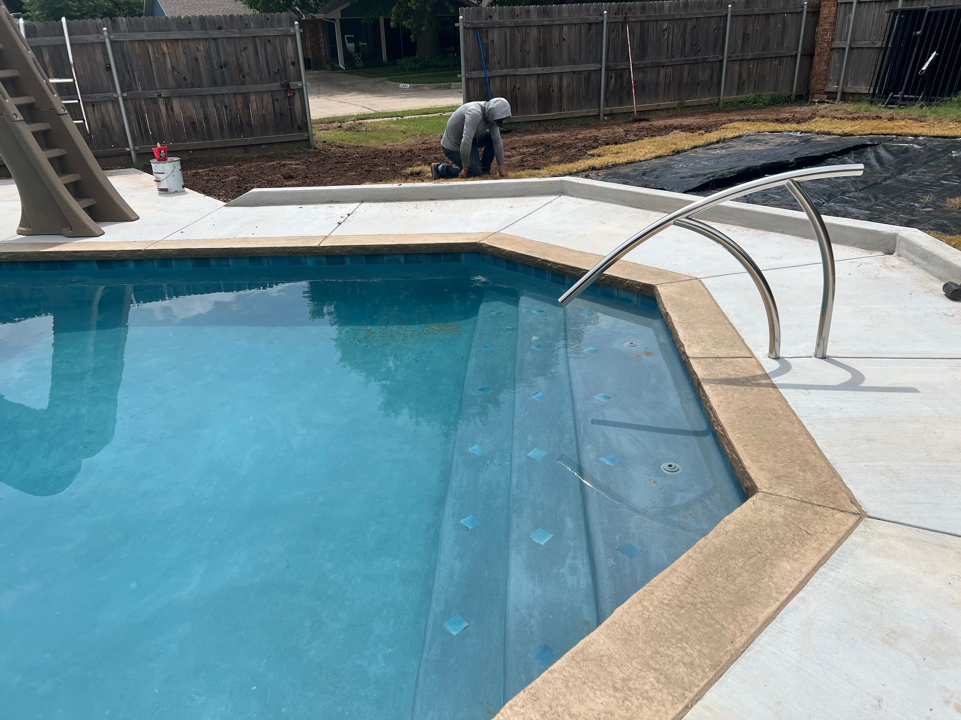 Backyard pool with a curved metal handrail and two workers near a wooden fence