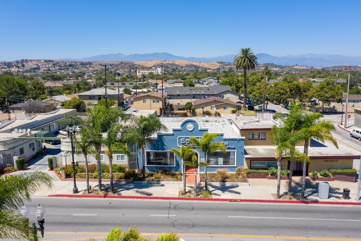 An aerial view of a building with palm trees on the side of the road.