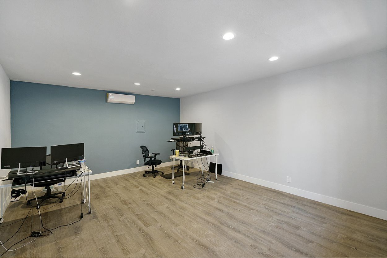 A room with a wooden floor and a blue wall has a lot of computers on the desks.