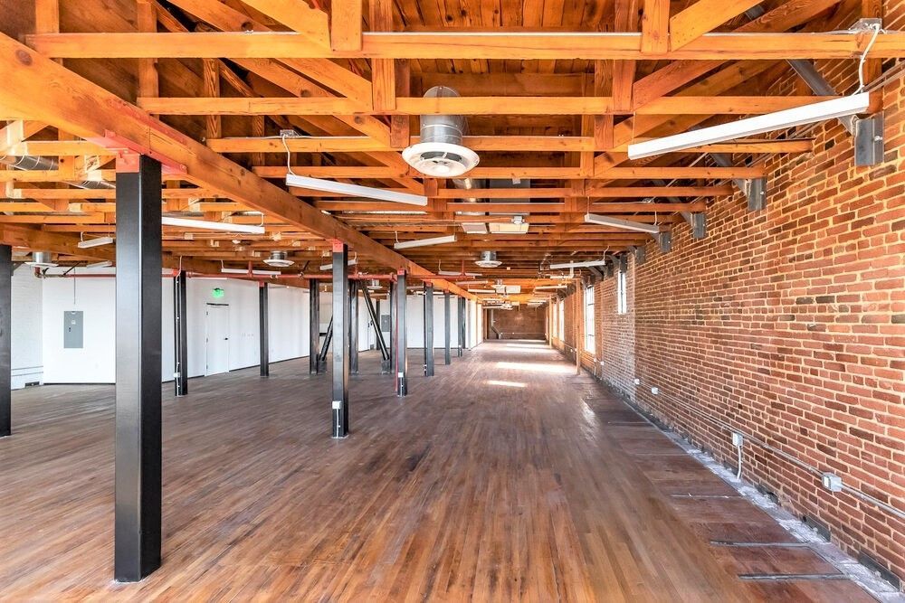 A large empty room with wooden floors and a brick wall.