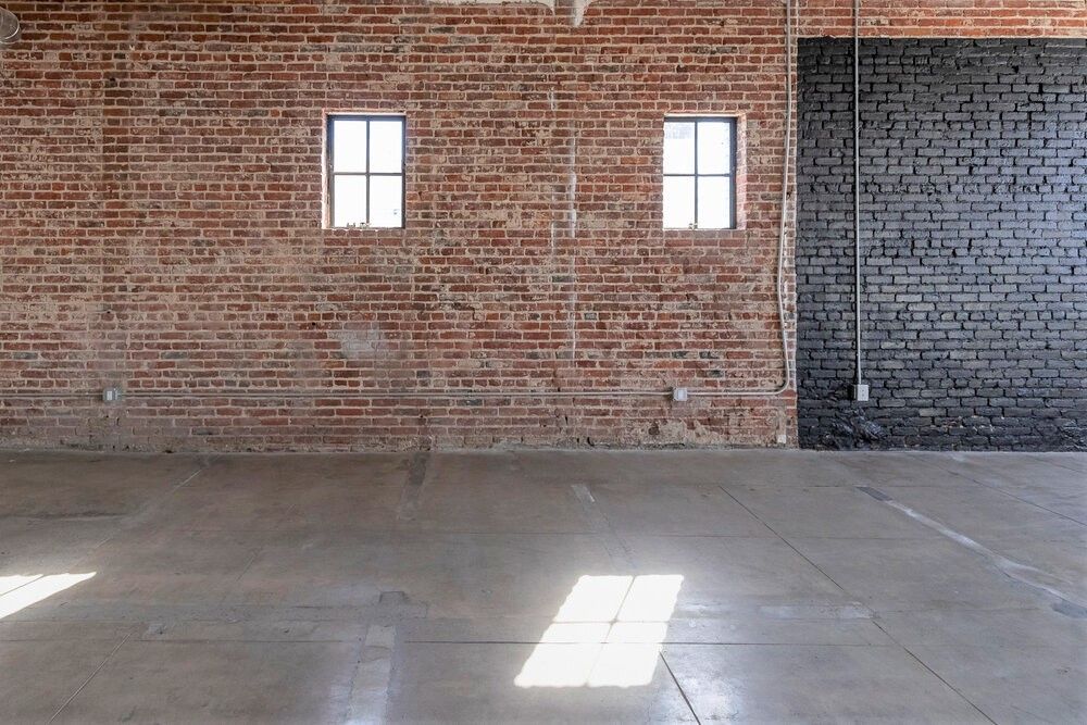 An empty room with a brick wall and two windows