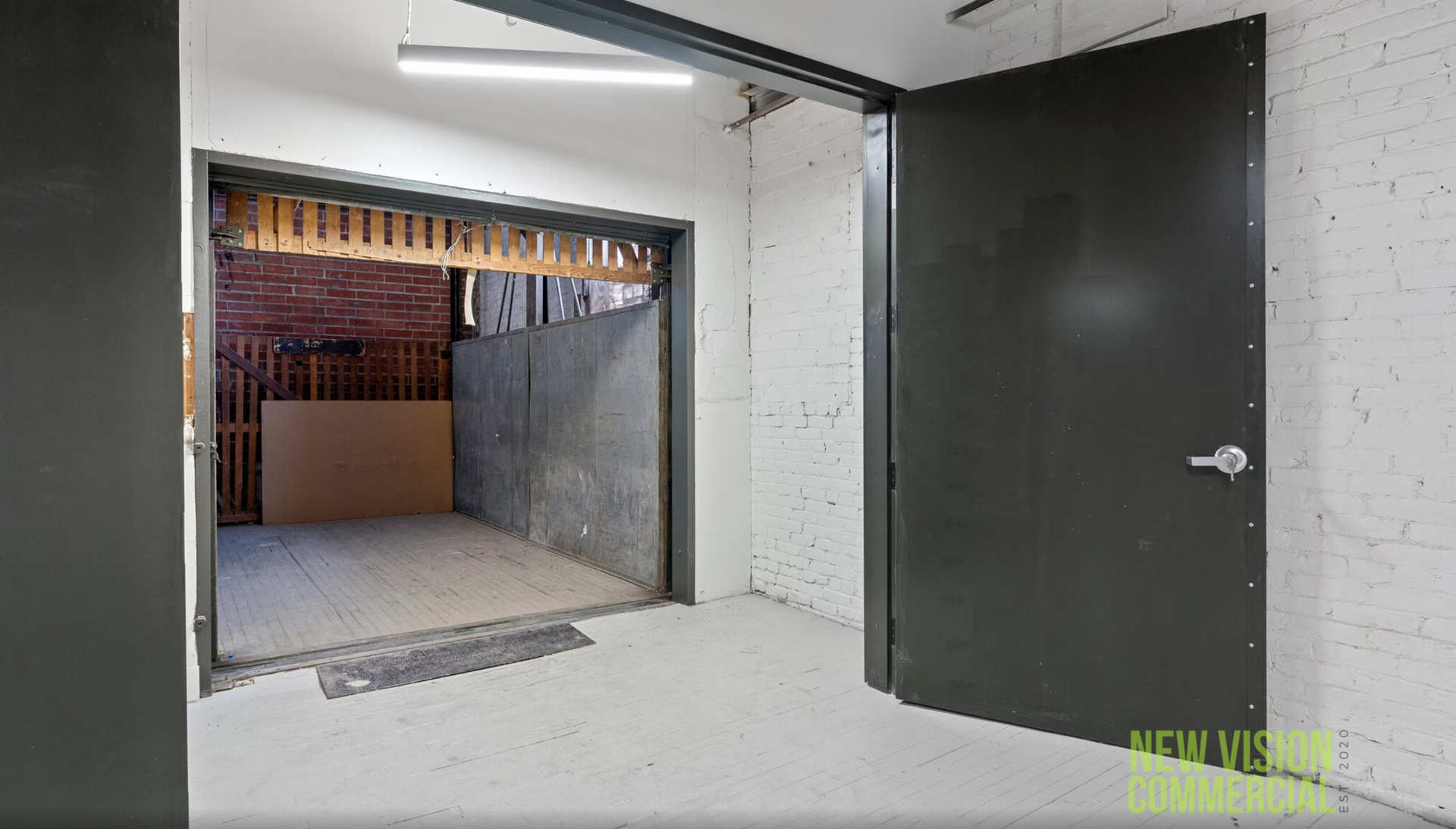 An empty room with a black door and a brick wall