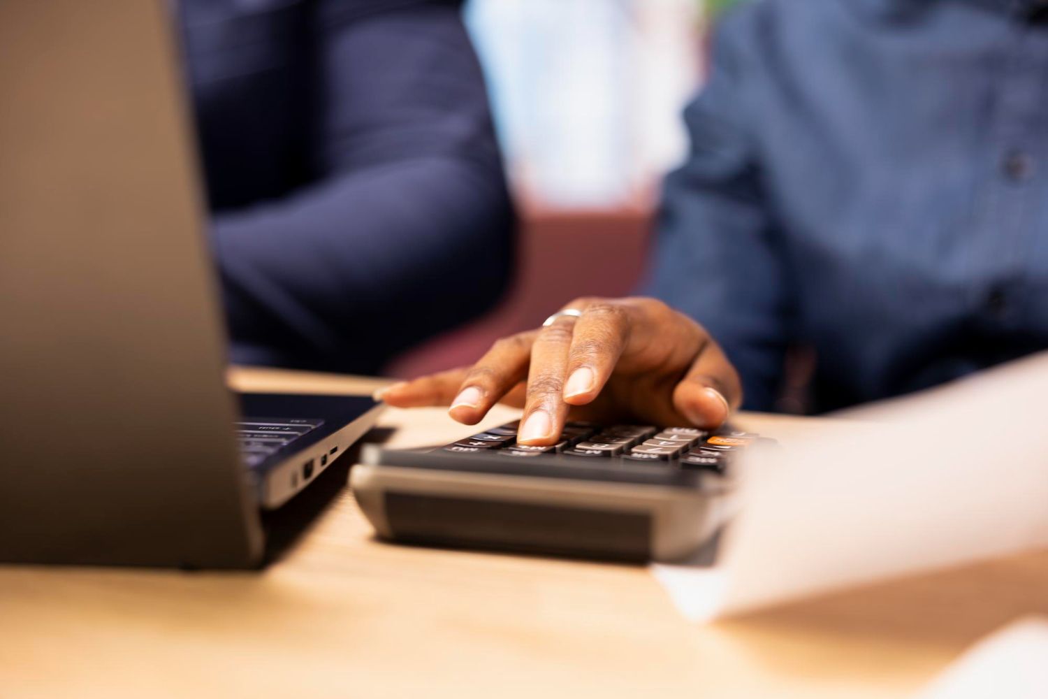 Person using a laptop and calculator at a desk with paperwork