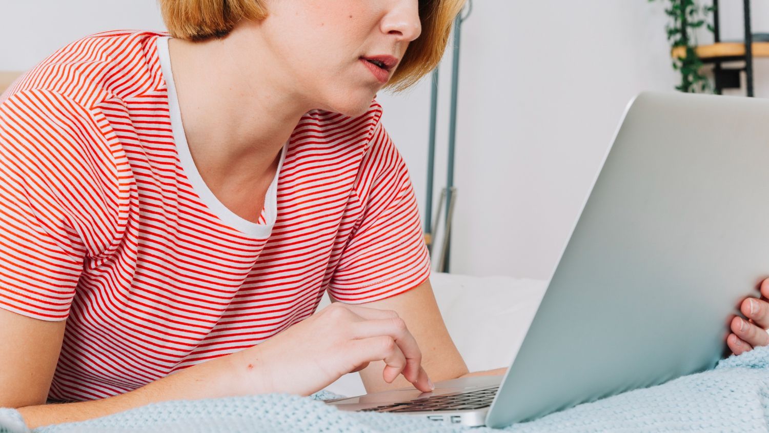 Person in a red striped shirt using a laptop on a bed