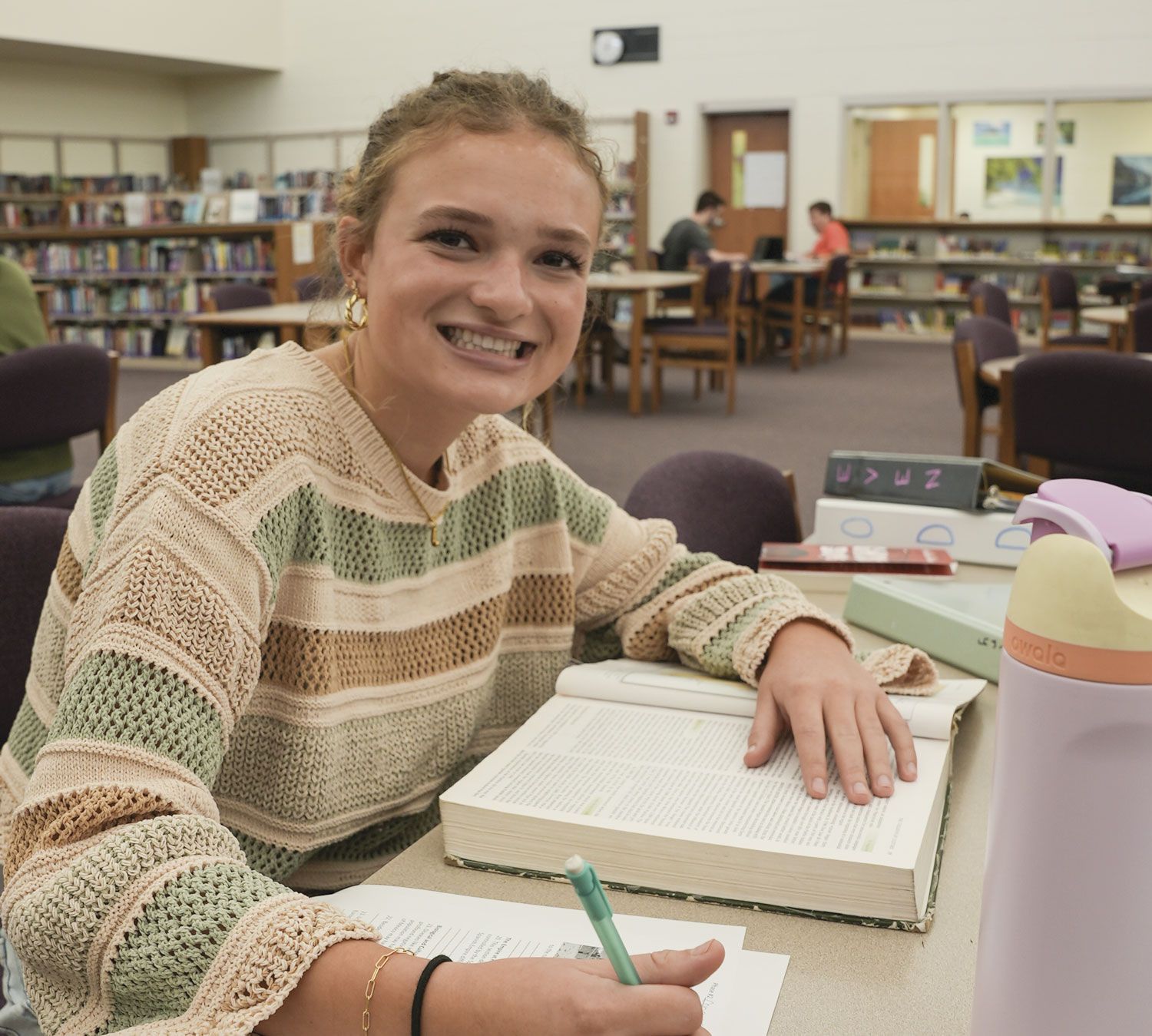 Smiling female student at a table in the Media Center, doing homework