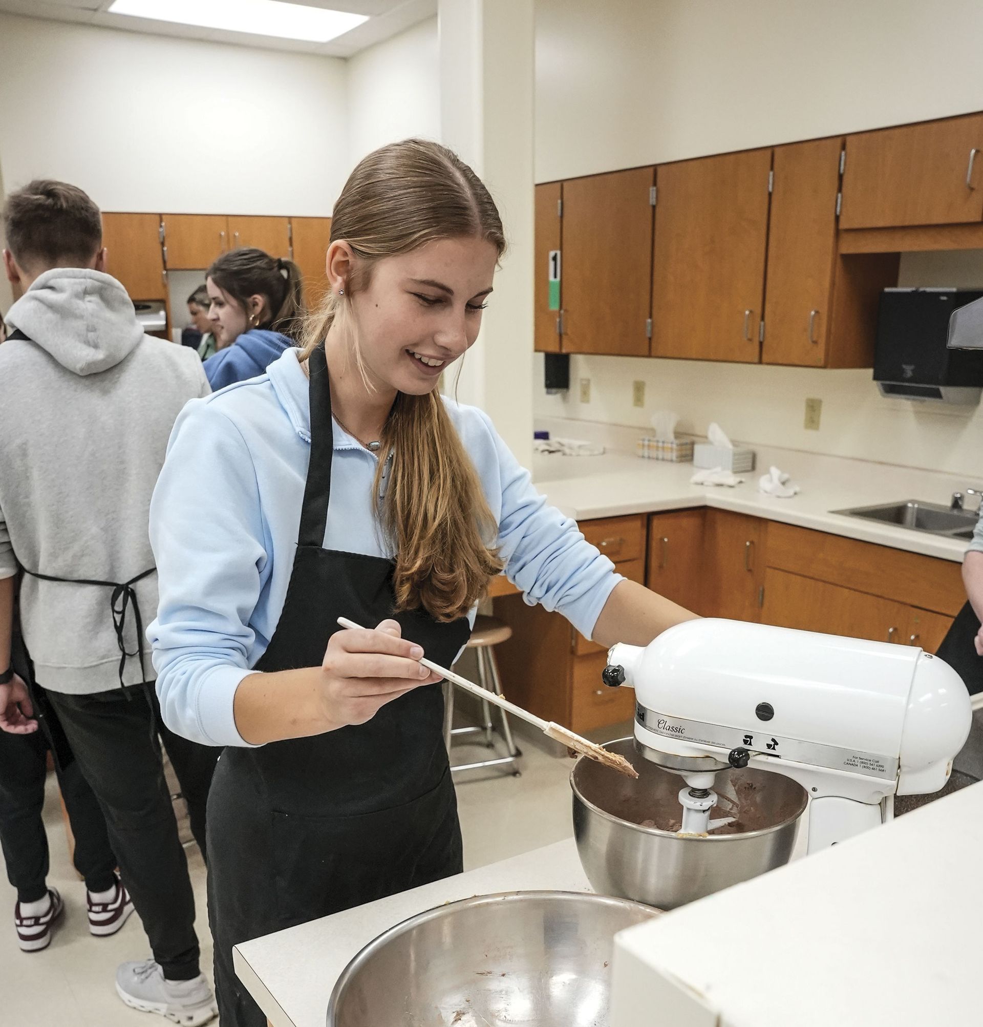 Female student in kitchen, smiling as she uses the mixer