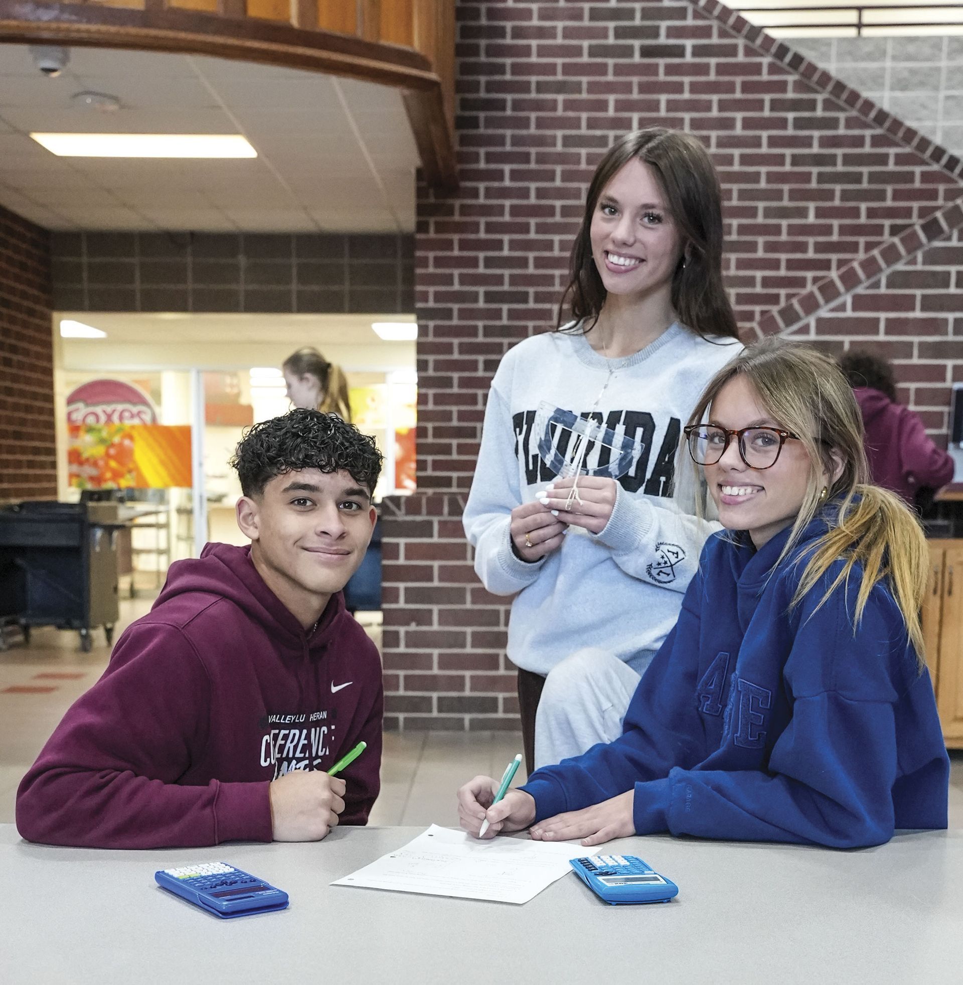 Two girls and one boy in Commons, at a table, smiling at camera