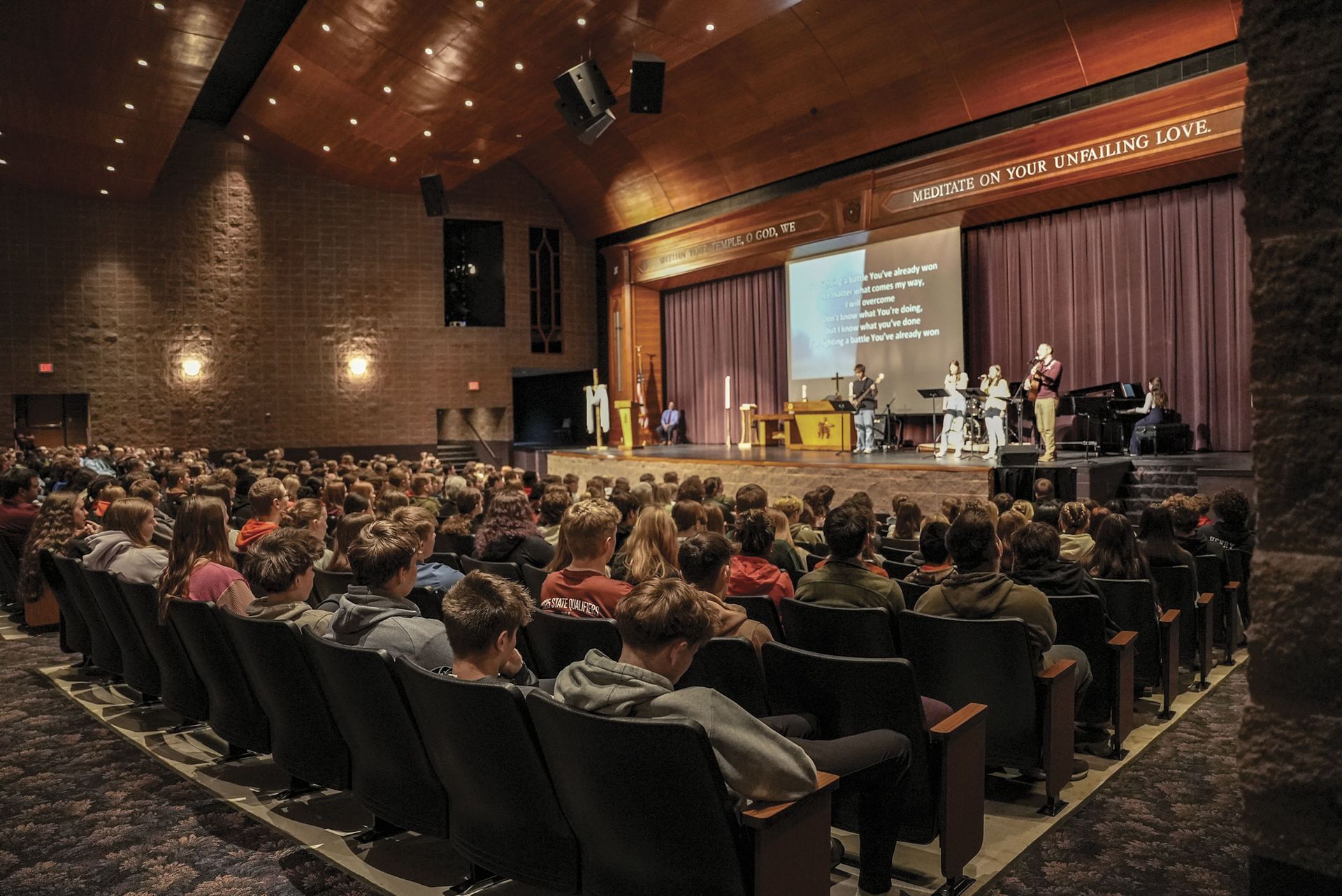 Full auditorium during chapel - photo from behind, over heads, looking at stage