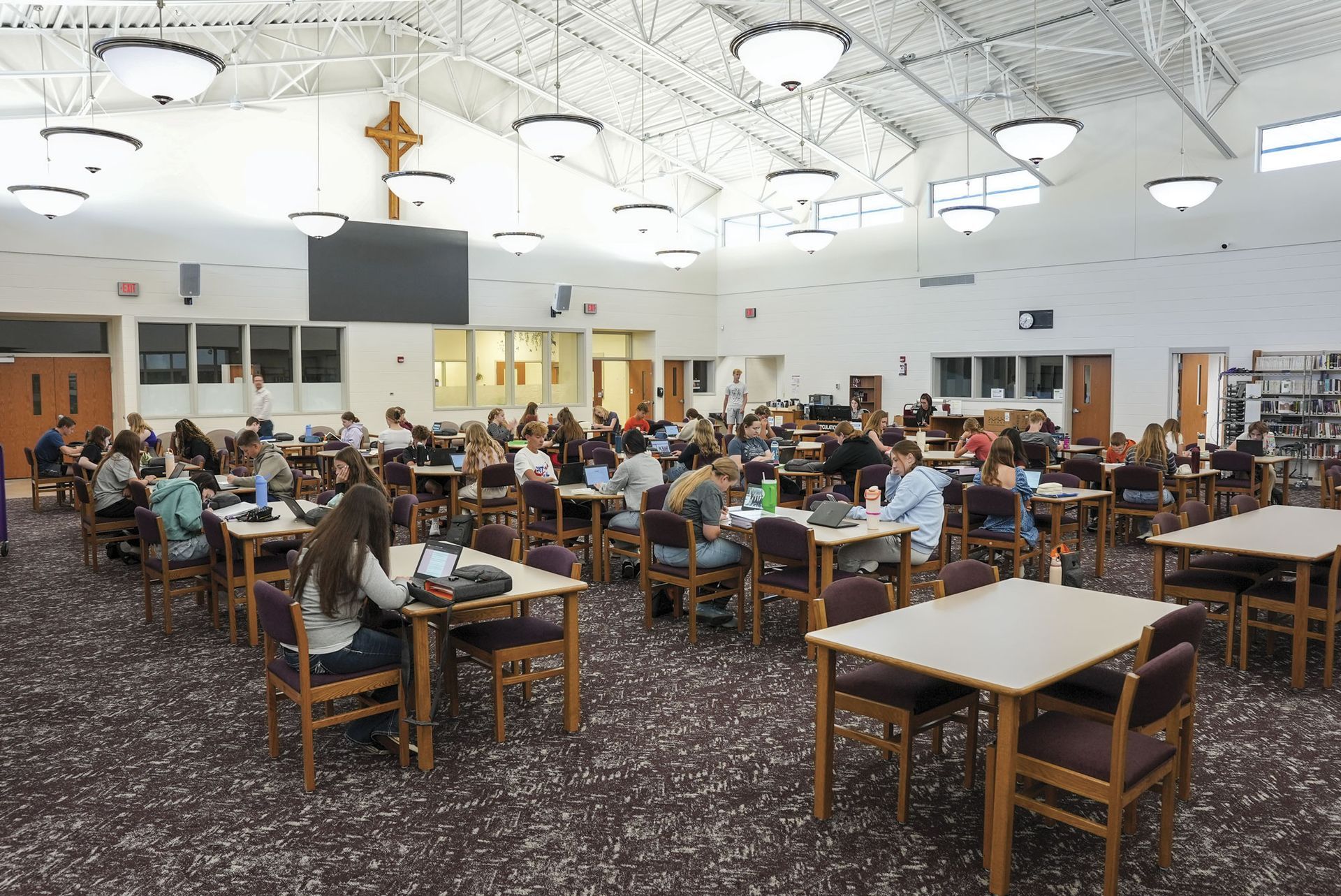 Media Center with high ceilings, a cross and screen on the wall, and students sitting at tables in the space.