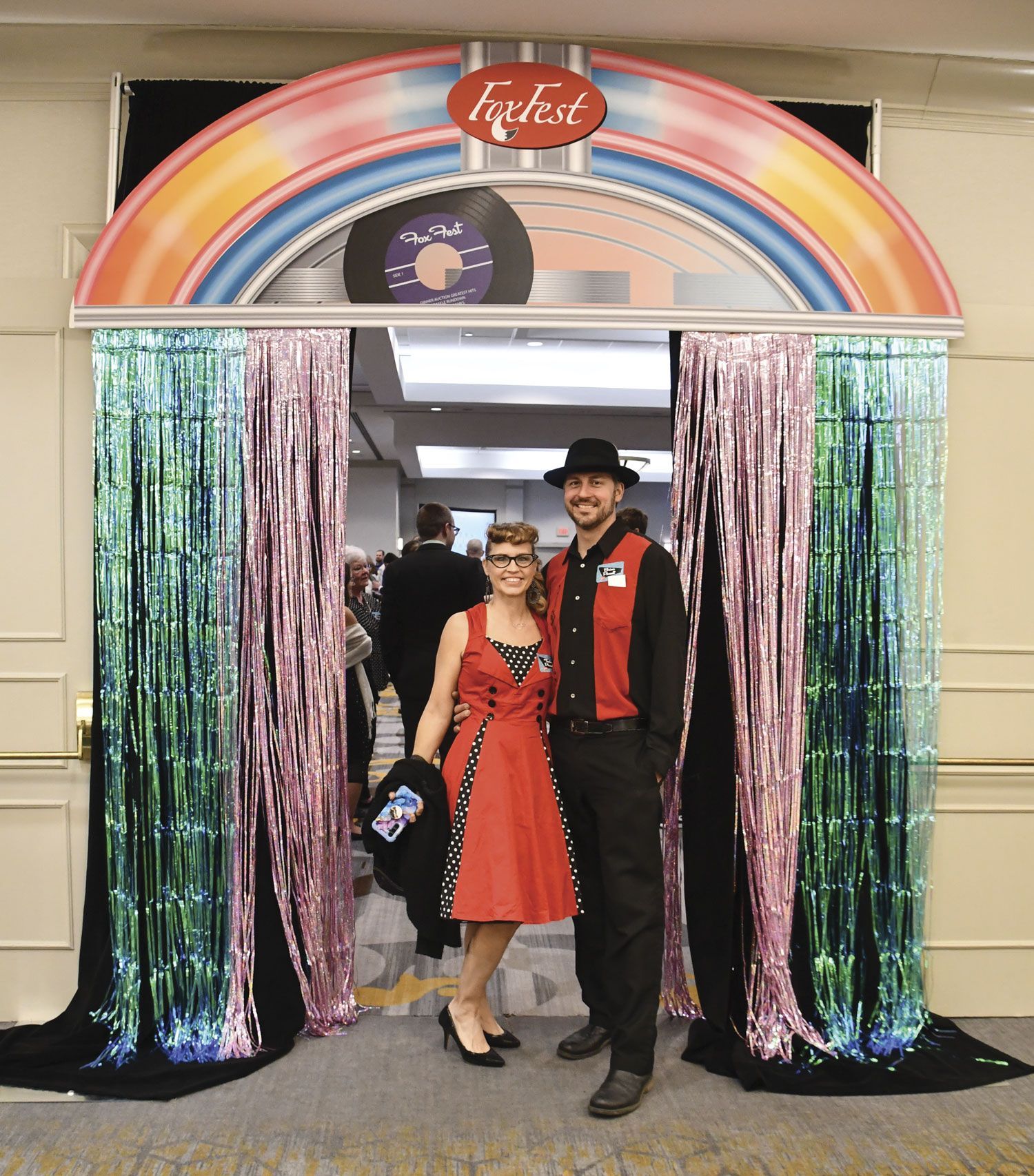 Couple  dressed in 50s clothing, smiling and standing in the jukebox entrance to the event