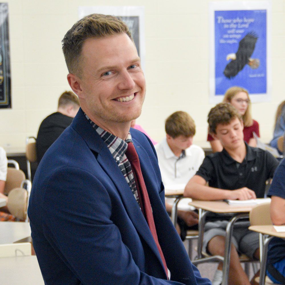 Joe Blum in study hall, smiling, and with students at desks in the background