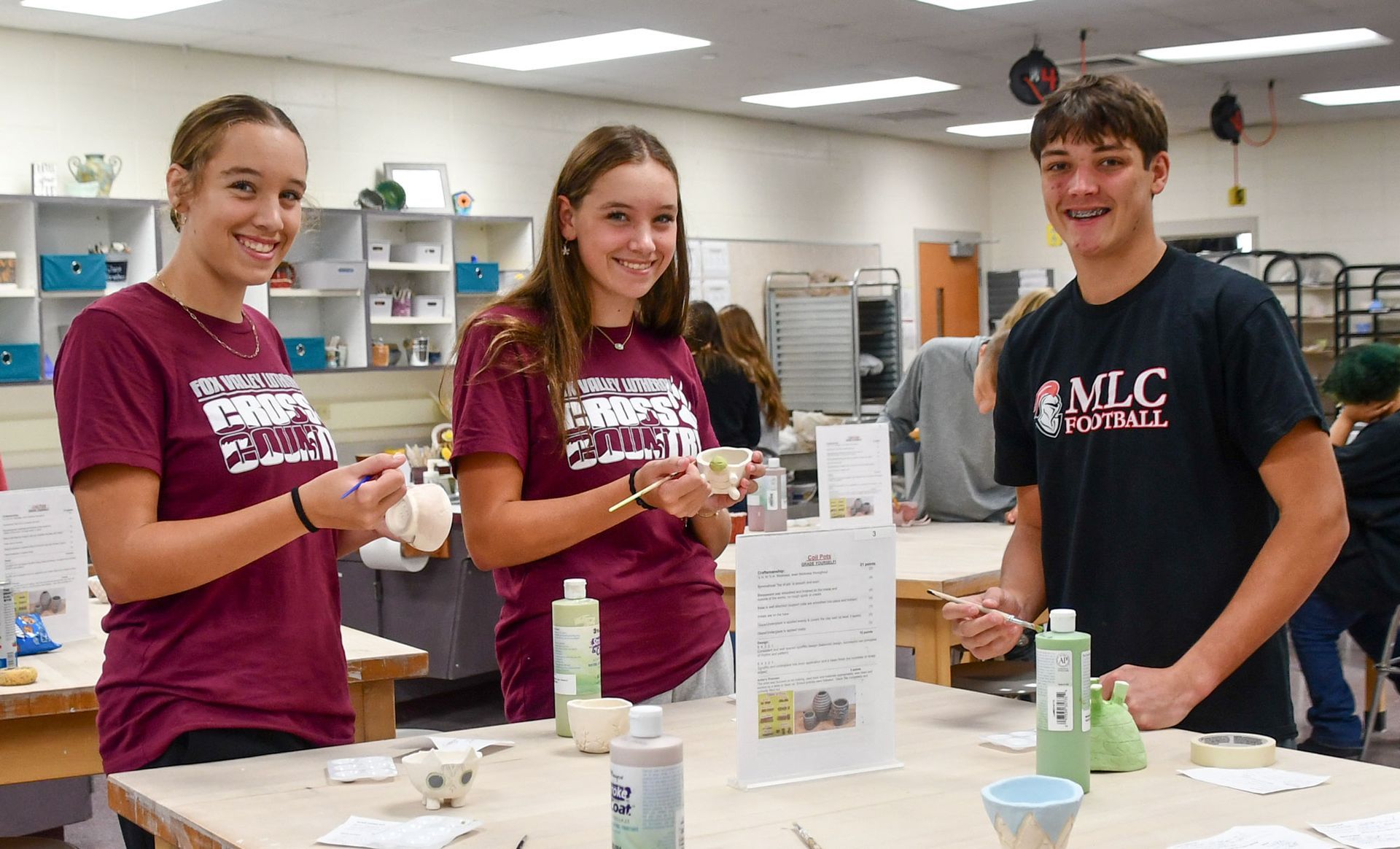 Smiling students (two females, one male), working on their ceramics projects.