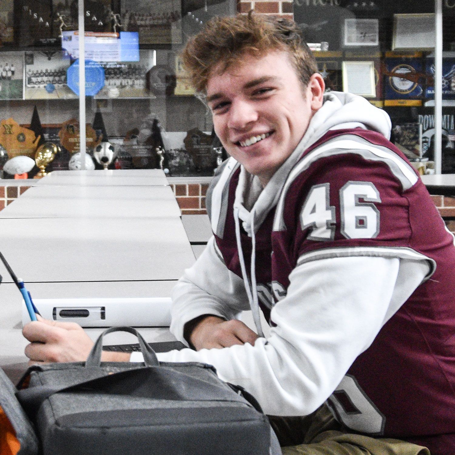 Smiling male student in Commons at a table with his laptop and trophy cases in the background