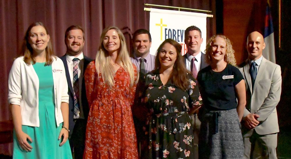 8 newly installed faculty smiling at the camera while on stage at FVL
