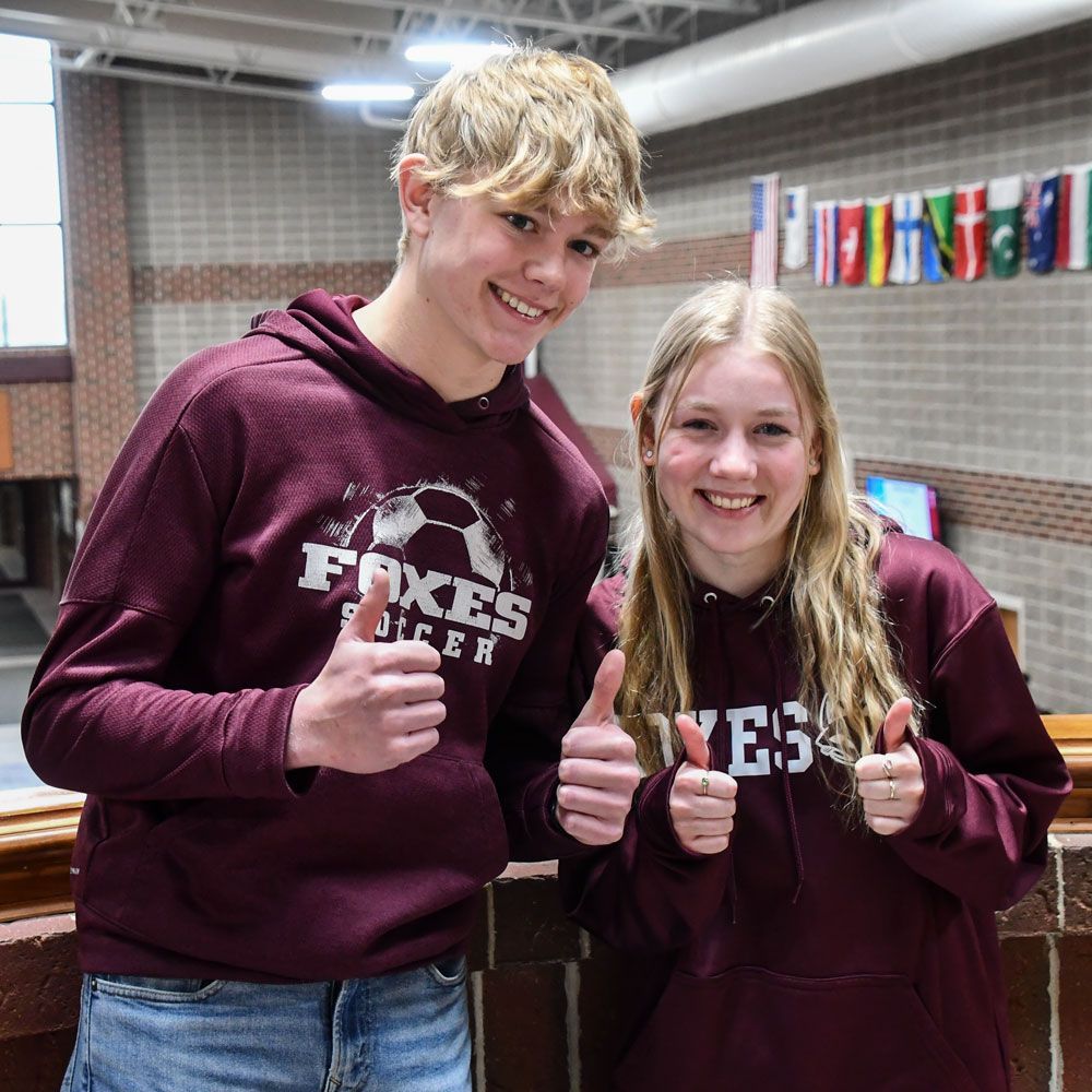 Happy boy and girl students with their thumbs up and the FVL Commons behind them. 