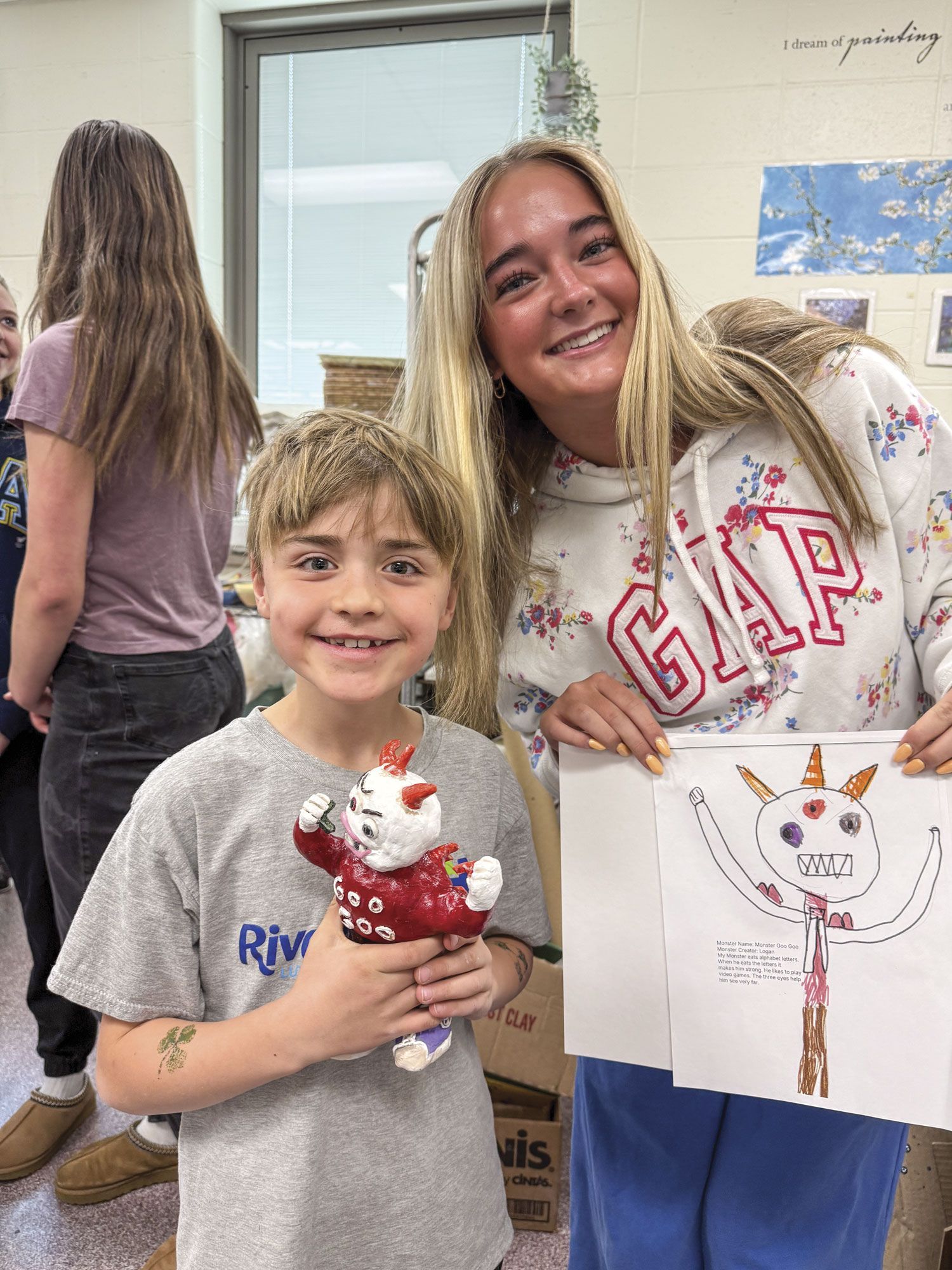 FVL student holding monster drawing, and smiling 1st grader holding finished monster