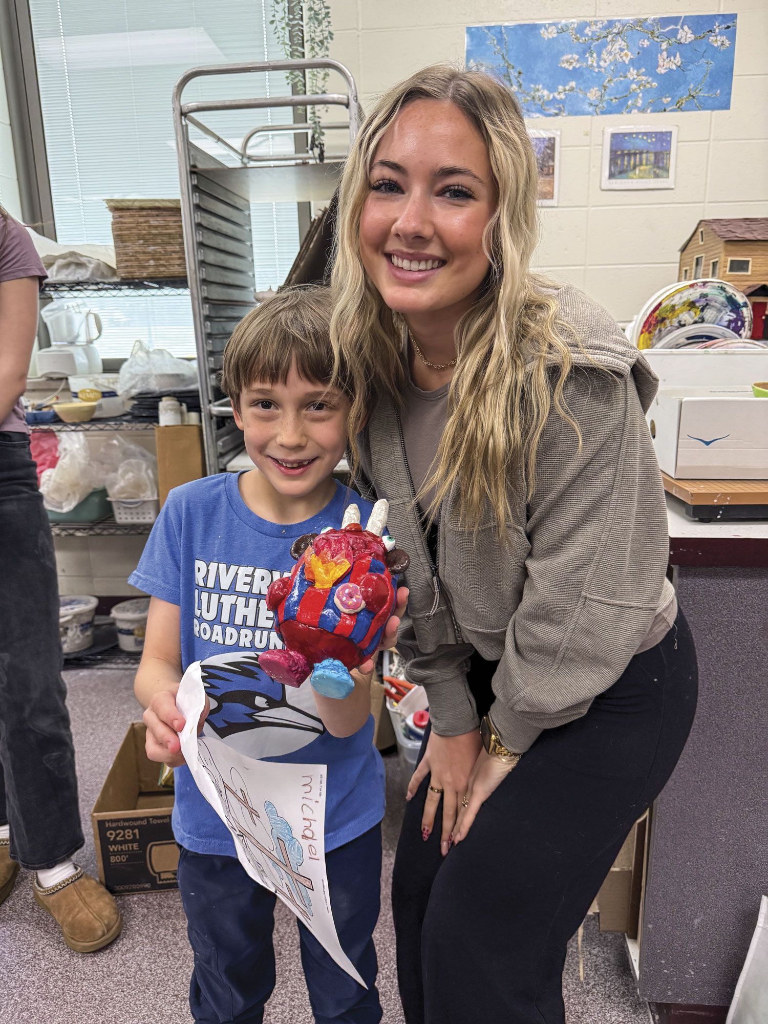 Smiling FVL student and 1st grader. 1st grader is holding his completed ceramic monster