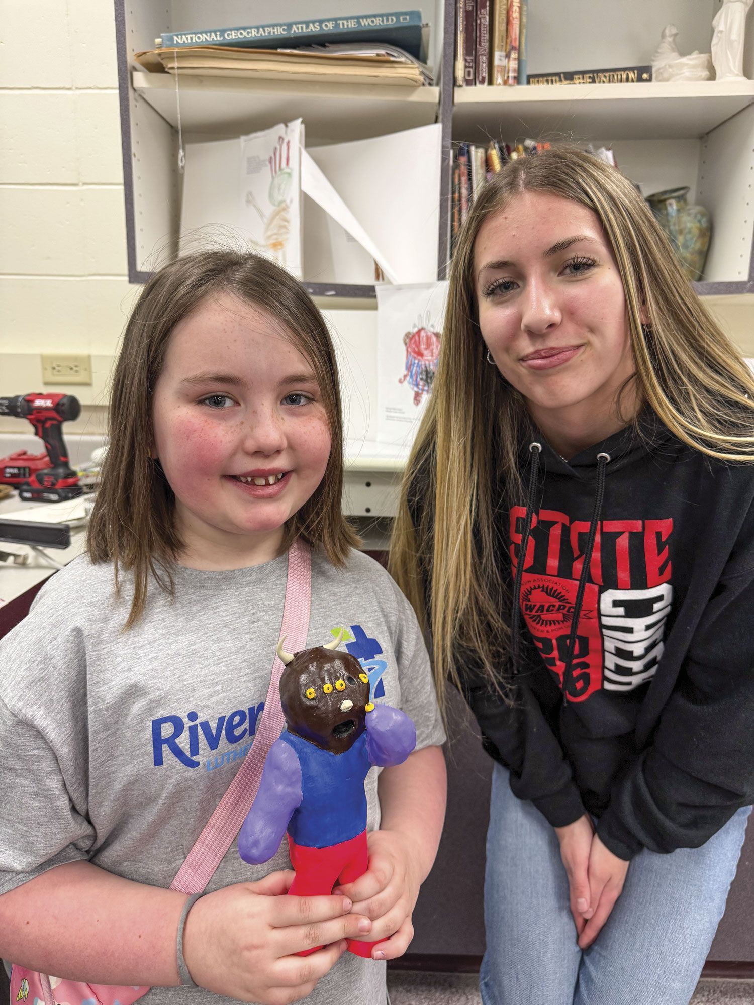Female FVL student with smiling 1st grader who is holding her ceramic monster