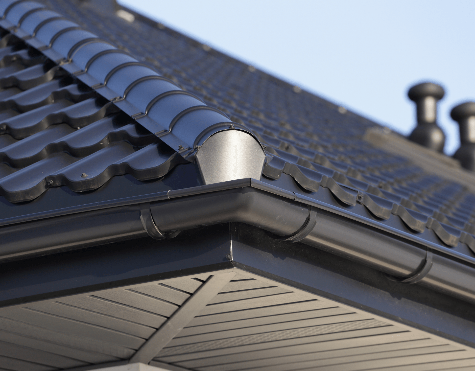 Close-up of a dark blue tiled roof with a gutter and white soffit under a clear sky