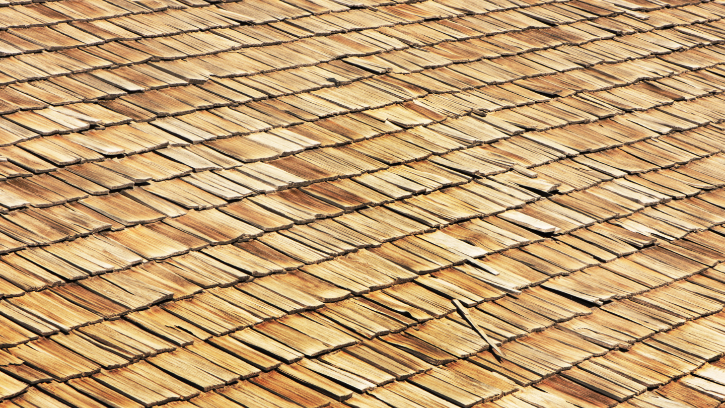 Worker pressure-washing a red tiled roof beside a brick chimney under a blue sky