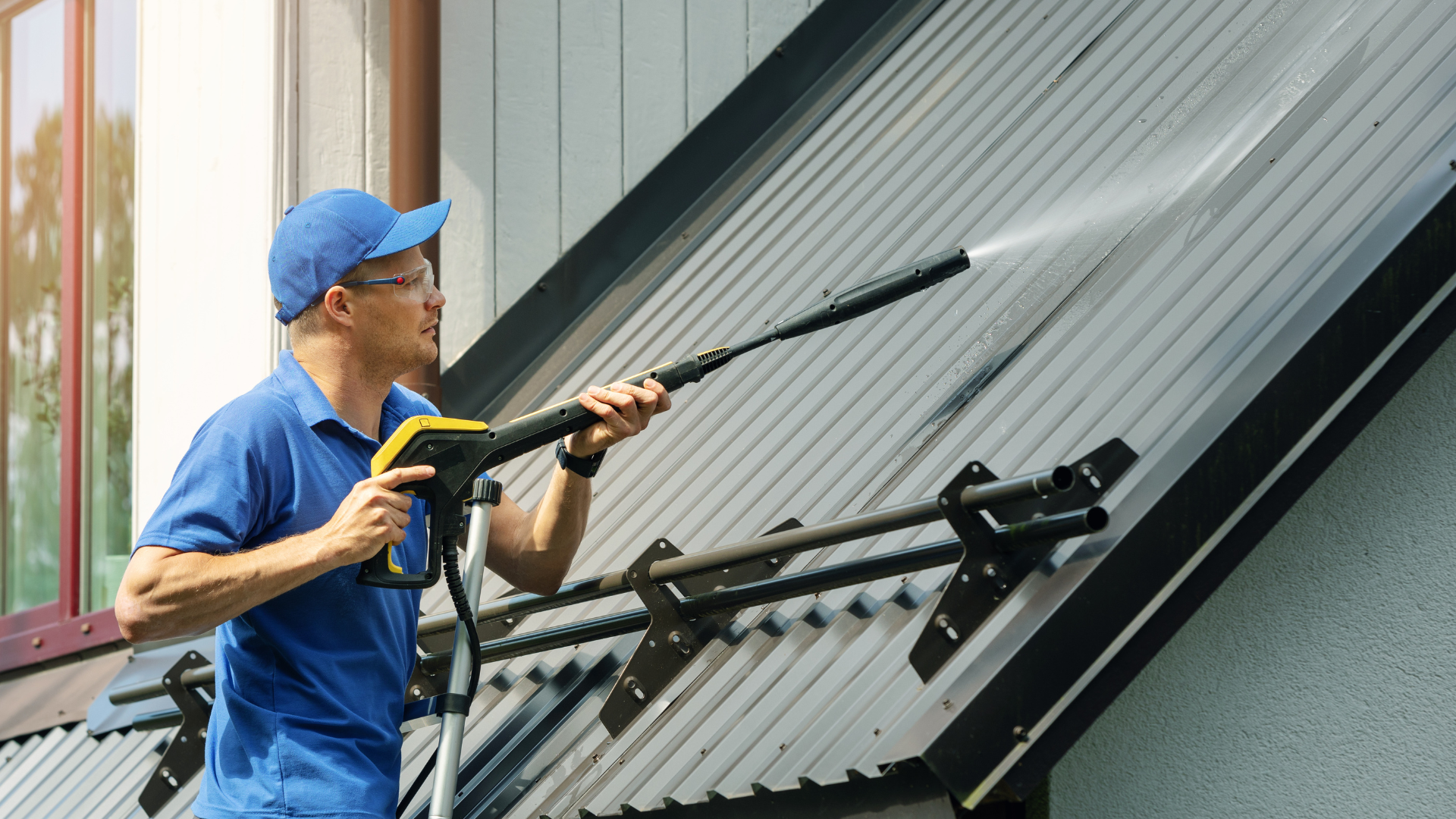 Worker in a yellow hard hat inspecting roof shingles on a sloped roof