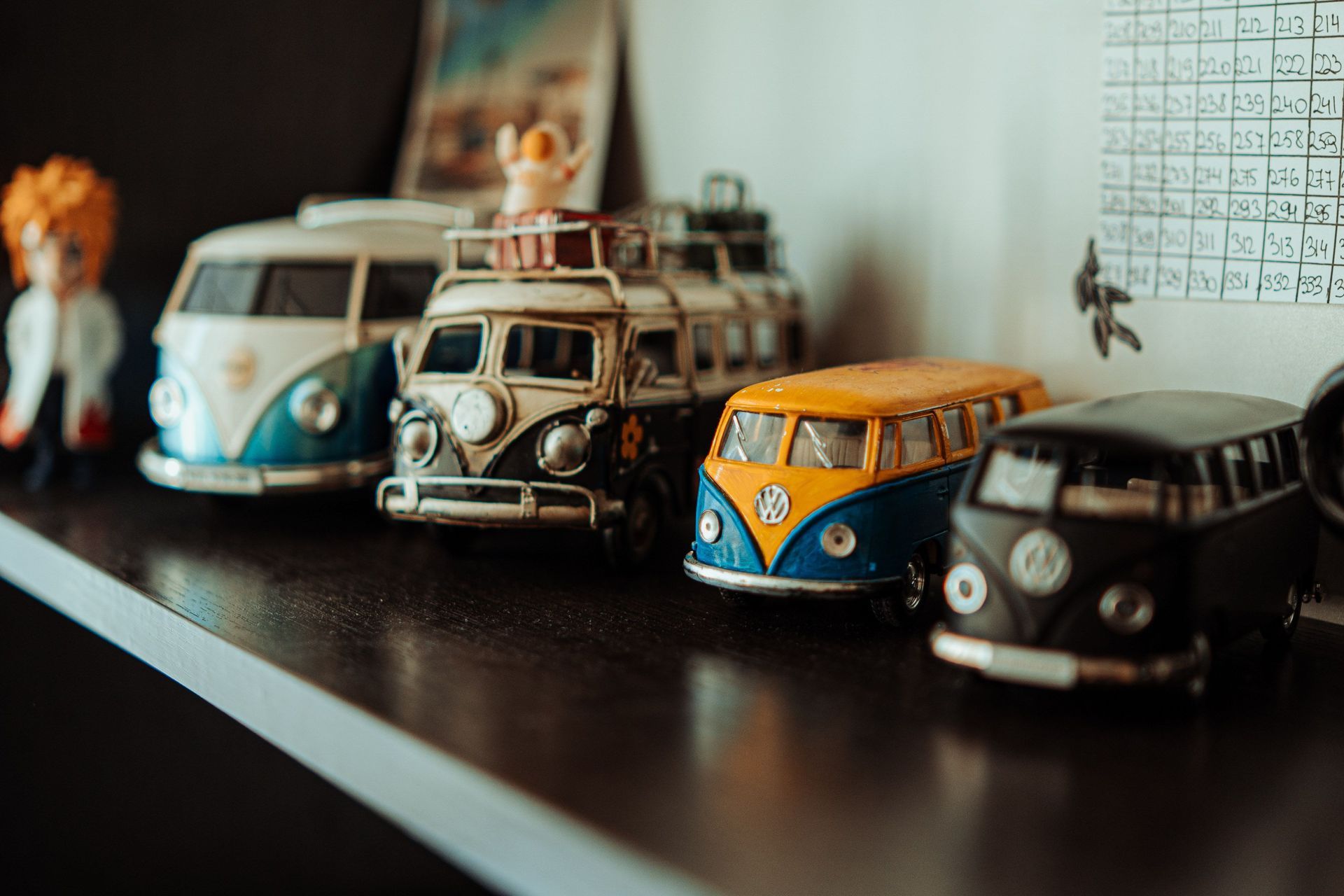 Row of colorful toy vans on a shelf, including blue, yellow, black, and white models